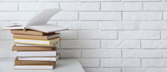 Stack of different books on table near light brick wall