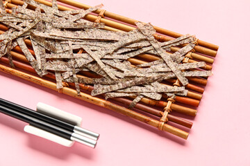 Bamboo mat with cut nori sheets on pink background, closeup