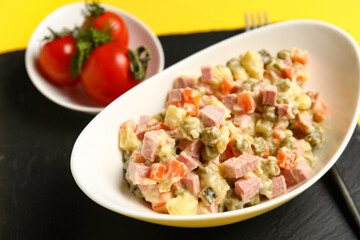Bowl of tasty Olivier salad on yellow background, closeup