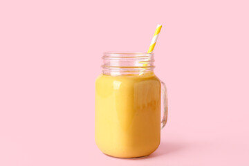 Mason jar of tasty yellow smoothie with straw on pink background
