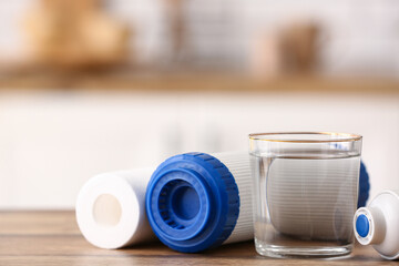Glass of water with filters on wooden table in kitchen