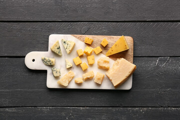 Board with pieces of tasty cheese on dark wooden background