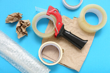 Adhesive tape rolls, dispenser, bubble wrap and paper on blue background