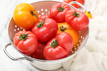 Colander with different fresh tomatoes on white background