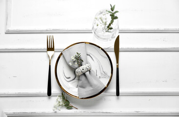 Plate with folded napkin, gold cutlery and glass on wooden white background