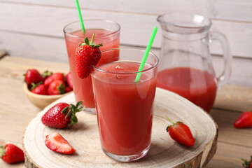 Jug and glasses of tasty strawberry juice on wooden table