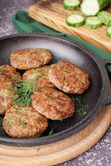 Frying pan with cutlets, dill and wooden board on grey grunge table in kitchen