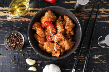 Tasty sweet and sour chicken in bowl with spices on dark wooden background