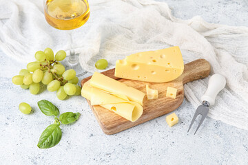 Wooden board with tasty Swiss cheese and grapes on light background