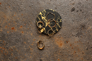 Decorative podium with beautiful golden rings and earrings on grunge brown background