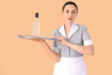 Female waitress with bottle of vodka on beige background