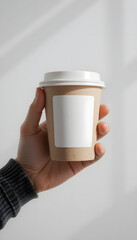 A hand holding a paper coffee cup mockup with a blank white label.