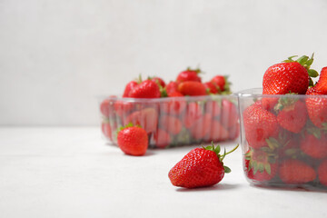 Plastic containers with fresh strawberry on light background, closeup