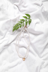 Beautiful pearl necklaces with plant leaves on white cloth