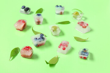 Frozen berries in ice cubes and leaves on green background