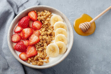 Healthy yogurt bowl with granola, fresh strawberries, and banana slices, topped with honey