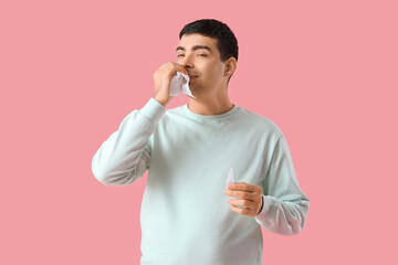 Ill young man with tissue and nasal drops on color pink
