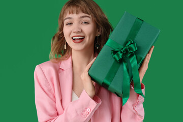 Beautiful young woman with gift box on green background