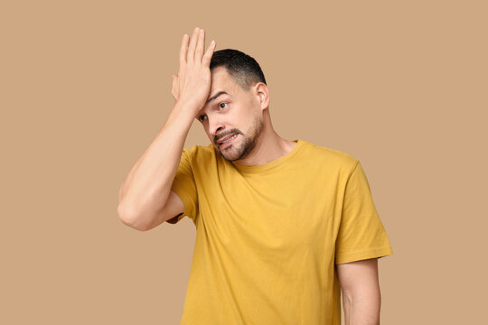 Handsome ashamed young man covering face with hand on brown background