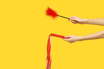 Female hands with feather stick and and whip from sex shop on yellow background