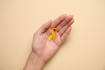 Female hand with golden awareness ribbon on beige background. International Childhood Cancer Day