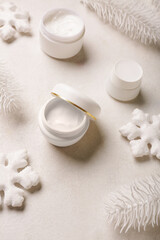 Jars of cream with decorative snowflakes and fir branches on white background