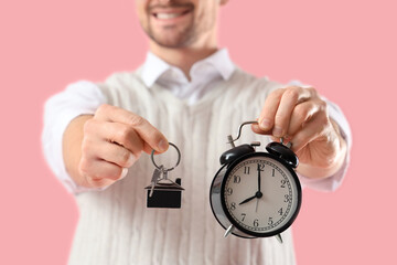 Male real estate agent with keys and alarm clock on pink background, closeup