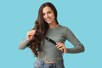Beautiful young woman with curling iron on blue background