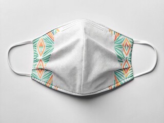 A disposable face mask features a white center and geometric patterns in green, orange, and blue on the sides.