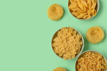Bowls with different tasty uncooked pasta on green background