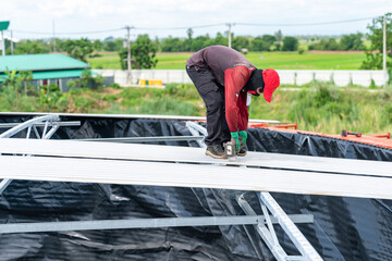 A worker is using a cordless screwdriver to remove screws from the metal sheet roof of the silo.