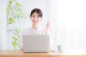 パソコンの前でカメラ目線の笑顔の女性　オフィスカジュアルのイメージ　ピンクのシアーシャツのかわいい女性	　ガッツポーズ