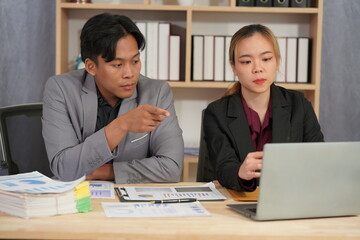 Businessman and woman working together on project using laptop and documents. Busy business people reviewing documents, reading financial reports, talking, working together on laptop computers.