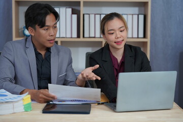 Businessman and woman working together on project using laptop and documents. Busy business people reviewing documents, reading financial reports, talking, working together on laptop computers.