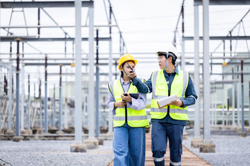 Two engineer working at high voltage power substation performing inspection and check on infrastructure with safety helmet and vest for secure environment and efficient operation