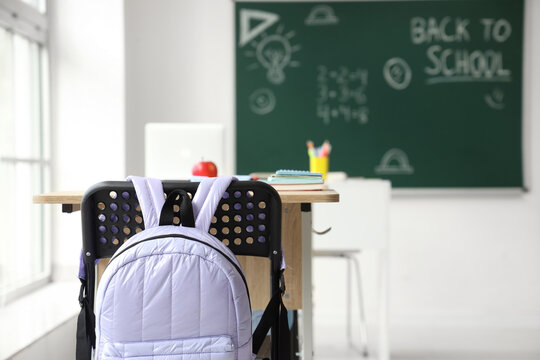 Interior of empty classroom with school desks and text BACK TO SCHOOL on chalkboard