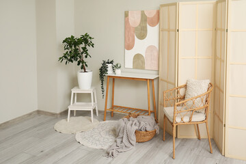 Table, comfortable armchair and folding screen in interior of stylish living room