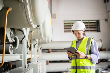 Engineer wearing safety helmet and insulated vest inspects electric grid field using tablet near...