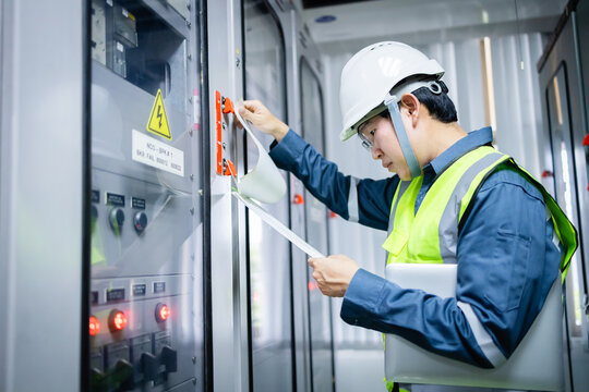 Electrical engineer is performing inspection in substation control room with control panel, ensuring safety and functionality with focused attention and protective gear