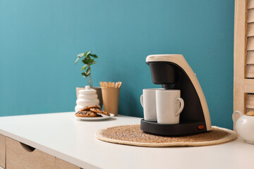 Coffee machine with cups on table near blue wall, closeup