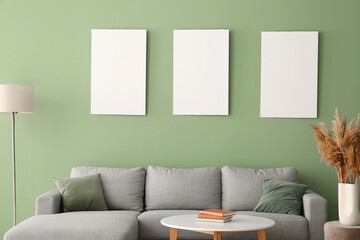 Comfortable sofa, table and blank posters on green wall in room