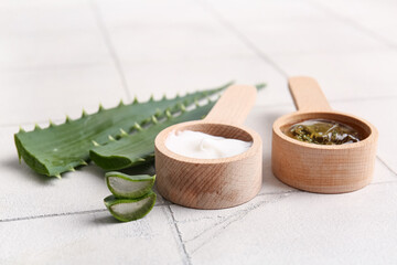 Wooden spoons of cosmetic cream and gel with aloe vera leaves on white tile background, closeup