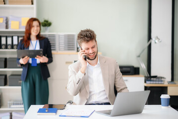 Obraz premium Two business workers talking on the smartphone and using laptop at office.