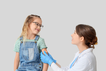 Little girl with doctor applying patch after vaccination on light background