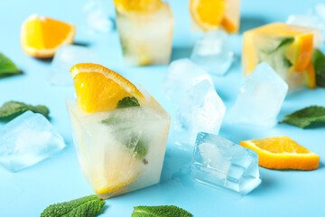 Ice cubes with fresh orange and mint leaves on blue background, closeup
