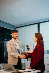 Fototapeta premium Two business professionals shaking hands in an office, symbolizing partnership, success, and teamwork.
