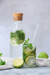 Glass and bottle of fresh Mojito cocktail with mint on grey background