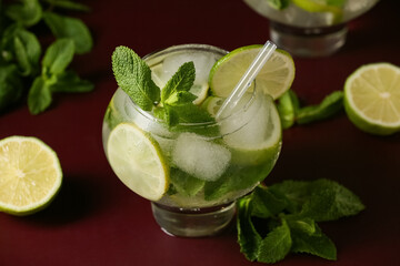 Glass of fresh Mojito cocktail with lime and mint on red background, closeup