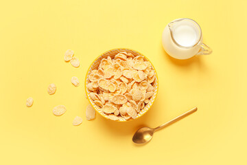 Composition with bowl of tasty cornflakes and jug of milk on yellow background