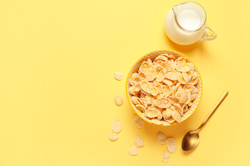 Composition with bowl of tasty cornflakes and jug of milk on yellow background